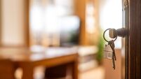 House keys with house shaped keychain hanging on a door, opening to a new home, representing real estate investment, purchase, m