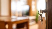 House keys with house shaped keychain hanging on a door, opening to a new home, representing real estate investment, purchase, m