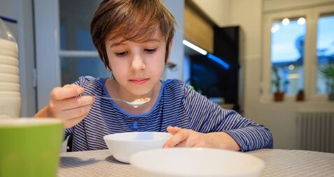 Preadolescent boy having cereal with milk for breakfast at the dining table at home