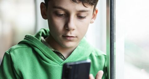 Boy with smartphone indoors. Preteen boy using a phone checking social media. Concept of children using the smartphone
