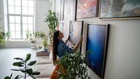 iStock-2213326166.jpg Talented female artist hangs finished modern painting on wall in light spacious creative studio.