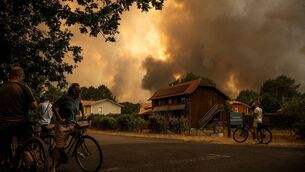 <p>Residents on their bicycle look at smoke rising behind a residential area during a wildfire near Lege-Cap-Ferret, southwestern France this July. File picture: Julien De Rosa/Getty</p>