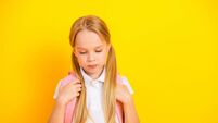 Portrait of a young schoolgirl in a white shirt carrying a pink backpack against a vibrant yellow background