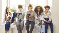 Children sitting on windowsill, playing online games on mobile phones and ignoring each other