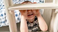 Child Smiling While Hiding behind a Wooden Staircase Inside a Cozy Room