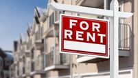 For Rent Real Estate Sign In Front of a Row of Apartment Condominiums Balconies and Garage Doors.