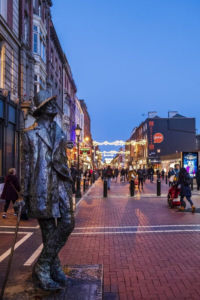 The life-size bronze statue of novelist James Joyce, installed by sculptor Marjorie Fitzgibbon in 1990, welcomes people in North Earl Street decorated for Christmas. It is located near the very centre of Dublin, the capital city of Ireland. The life-size bronze statue of novelist James Joyce, installed by sculptor Marjorie Fitzgibbon in 1990, welcomes people in North Earl Street decorated for Christmas. It is located near the very centre of Dublin, the capital city of Ireland.