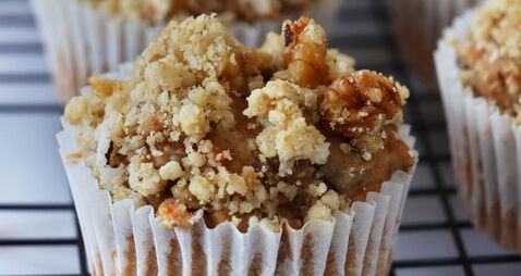 1318468128 Close-up image of rows of homemade apple muffins in paper cake cases topped with crumble on wire metal cooling rack, marble effe
