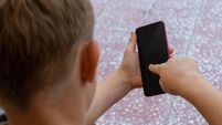 Young boy sitting outside holding a mobile or cellular smart phone. Connectivity, internet, millenial, screen time concepts.