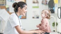 South Asian Female Nurse Smiles At Young Child During Clinic Visit