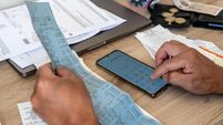 A person calculating the cost of living with a phone calculator and a desk full of bills and till receipts.