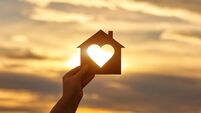 Woman hand holds wooden house in the form of heart against the sun