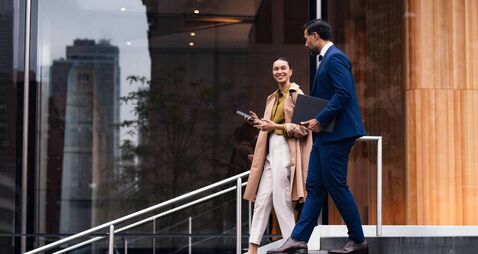 Professional Business Partners Descend Stairs Outside Modern Building in NYC, Carrying Folders and Tablet