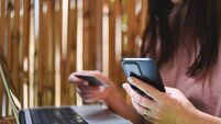 Woman using smartphone and credit card for online shopping on laptop