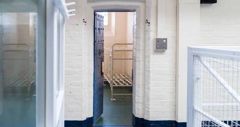 Looking in prison cell block victorian British English jail house with bed in room lock up high security room derelict old new c