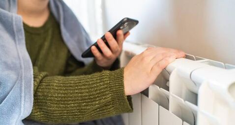 Young woman with smartphone near a radiator in winter