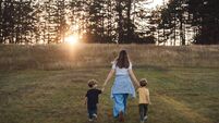Mother and her twin boys walking hand-in-hand through a grassy field at sunset
