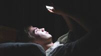 Depressed teenager on his phone in the dark.
