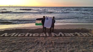 <p>Two Gazan students refused study visas in Ireland pose beside a sculpture of Taoiseach Micheál Martin's name, carved in the sand at Gaza.</p> <p>Two Gazan students refused study visas in Ireland pose beside a sculpture of Taoiseach Micheál Martin's name, carved in the sand at Gaza.</p>