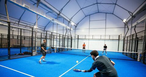 Group of skilled padel players playing padel match on new court indoors at night