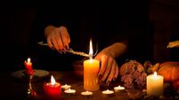 Witch make a spell on the altar in the dark. Female hands with sharp black nails burning magic herb among candles, pumpkin, nuts