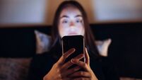 Teenage Woman relaxing in Bed using her Mobile Phone at Night