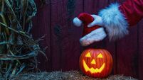 Santa placing a Santa Hat on a happy carved Jack O' Lantern on a hay bale with dried cornstalks