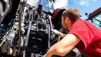 Low angle view of male agricultural machinery mechanic standing by farm tractor