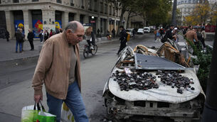 A man walks past a burned-out car in Paris after a quiet Monday night under curfew (Christophe Ena/AP/PA) A man walks past a burned-out car in Paris after a quiet Monday night under curfew (Christophe Ena/AP/PA)