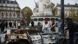 People examine a burned-out car after a quiet night on Monday under curfew in Paris (Christophe Ena/AP/PA)