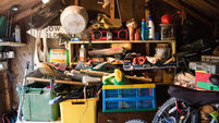 Inside a messy and cluttered wooden garage shed with tools, bikes and garden equipment piled up on uneven shelves in organised c
