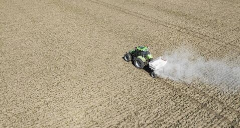 Tractor spreading agricultural lime in a field seen from above