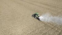 Tractor spreading agricultural lime in a field seen from above