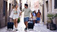 Happy couple of tourists dragging their suitcases on the street.