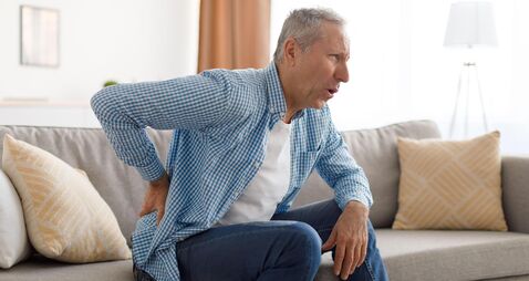 2HTJKC1 Mature man with side back pain sitting on couch at home