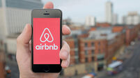 A man uses the Airbnb smartphone app while stood in a tall building overlooking a busy city street (Editorial use only)