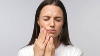 Young miserable woman experiencing severe toothache, pressing palm to cheek, closing eyes because of strong pain, isolated on gr