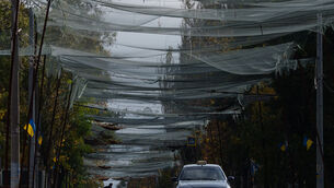 A local man rides a bicycle beneath anti-drone nets stretched over a street during a local ceasefire in Oleshky (Evgeniy Maloletka/AP) A local man rides a bicycle beneath anti-drone nets stretched over a street during a local ceasefire in Oleshky (Evgeniy Maloletka/AP)
