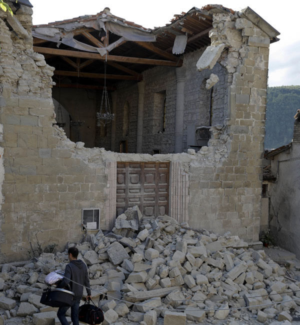 A man walks with a baby carry cot past a partially collapsed building after the earthquake in Accumoli. A man walks with a baby carry cot past a partially collapsed building after the earthquake in Accumoli.