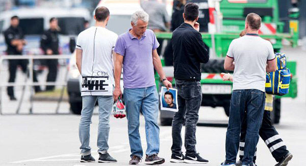 The father of a victim, centre, holds a picture of his son near the Olympia shopping centre. Pictures: AP