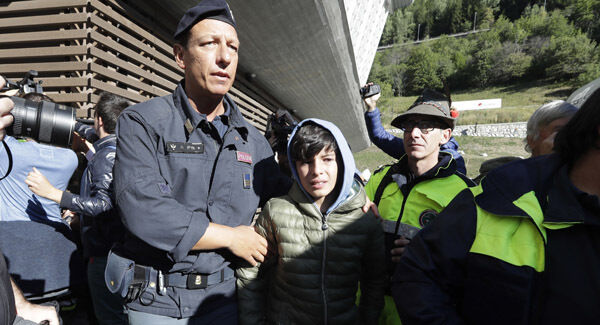An Italian police officer escorts a boy who was trapped overnight in cable cars above the Alps. Pictures: AP