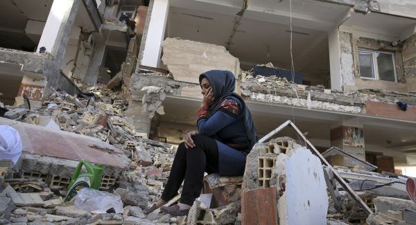 An earthquake survivor sits on debris in front of her house in a compound, which was built under the Mehr state-owned program