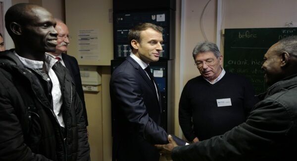 French President Emmanuel Macron shakes hands with migrant Salha Medhat, right, from Sudan, while migrant Attayet Ali, left, looks on during Macron&rsquo;s visit to a migrant center in Croisilles, northern France effectively place the British border in Calais.