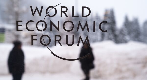 Two people walk behind the logo of the World Economic Forum at the meeting's conference center in&nbsp;Davos, Switzerland.