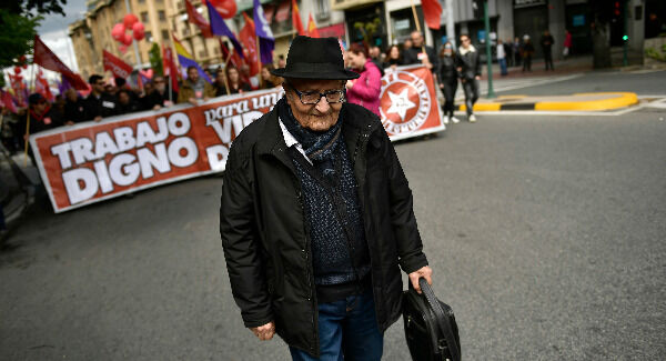 An elderly man walks in front of people holding a banner with writing reading "Decent work" and marching during a May Day rally in Pamplona, northern Spain. Pic: AP Photo/Alvaro Barrientos An elderly man walks in front of people holding a banner with writing reading "Decent work" and marching during a May Day rally in Pamplona, northern Spain. Pic: AP Photo/Alvaro Barrientos