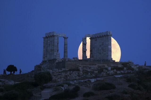 A full moon with a pinkish tinge rises behind the ancient temple of Poseidon in cape Sounio, about 40 miles south of Athens (Thanassis Stavrakis/AP)
