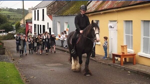 In ‘Turf Lights the Way!’ Kiskeam Brass band take a trip down memory lane in the north Cork village re-enacting a tradition where the band rehearsed marching through the village with pitchforks and lit sods of turf. It takes place at The Lane.