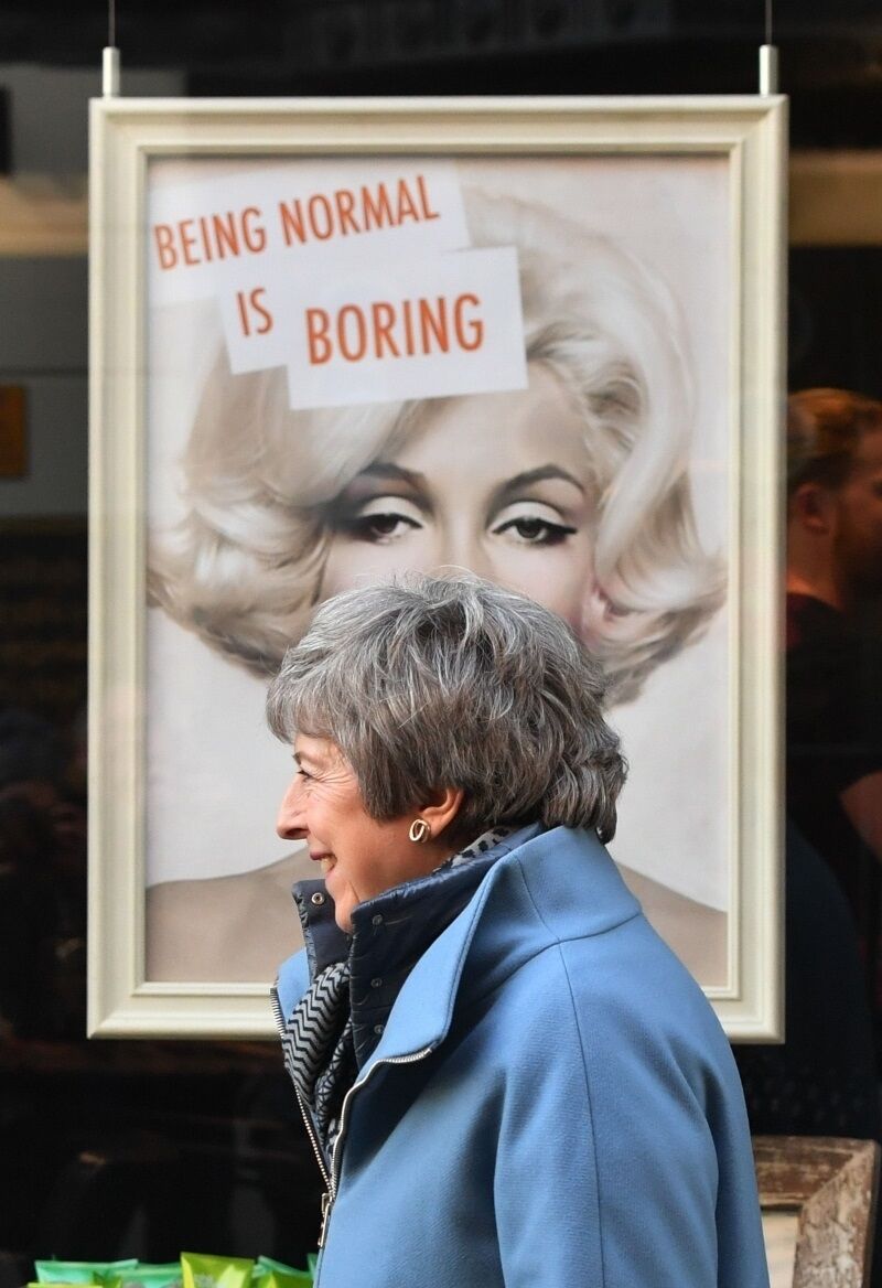 British Prime Minister Theresa May passes a display in a shop window while walking through Salisbury on the first anniversary of the Skripal poisoning today.