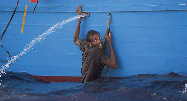 A man holds onto the side of a boat after jumping into the sea from an overcrowded wooden vessel in the Mediterranean yesterday.