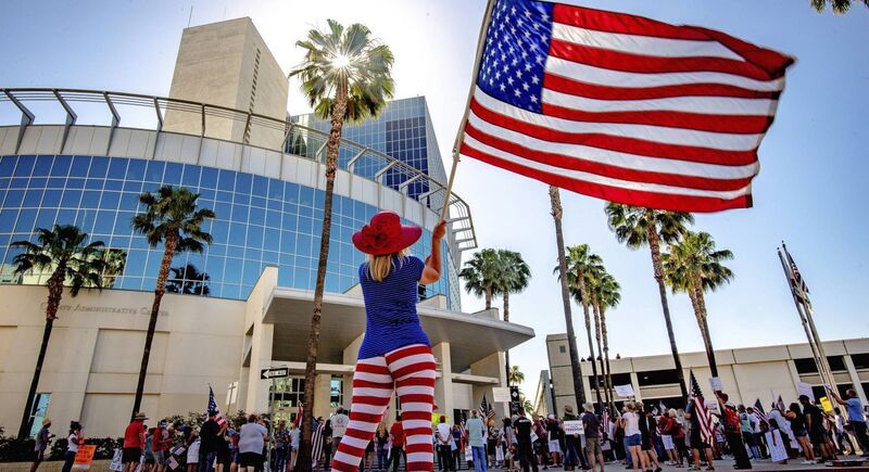 Tanya Acosta, of Highland, waves an American flag outside the Riverside County Administration building in Riverside, Calif. on Tuesday, May 5, 2020. as demonstrators protest to lift restrictions put in place due to COVID-19 outbreak. (Watchara Phomicinda/The Orange County Register via AP)